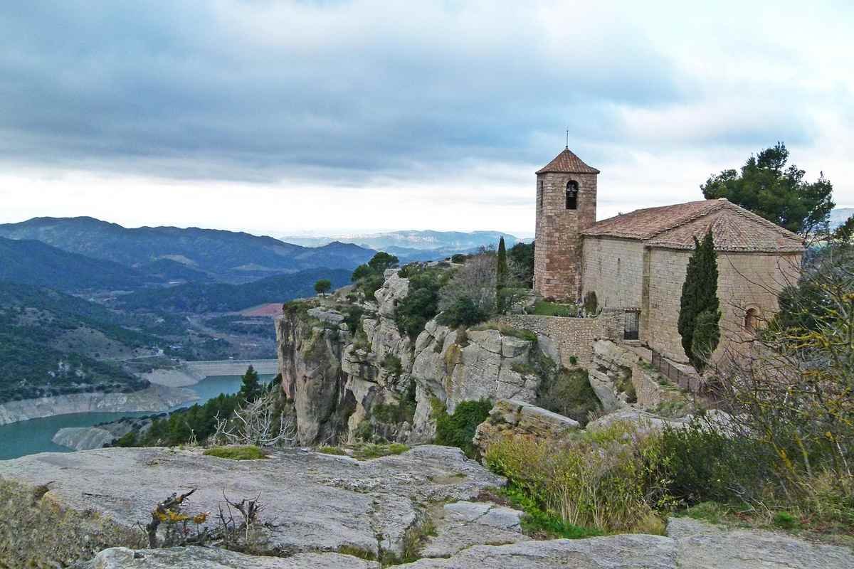 Église perchée sur une falaise avec vue sur une vallée et un ciel nuageux