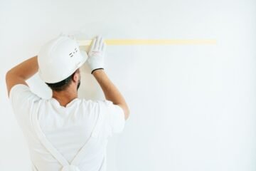 Un ouvrier en tenue blanche mesure un mur blanc avec un ruban