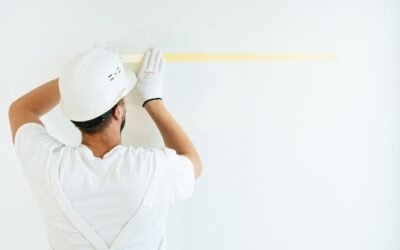 Un ouvrier en tenue blanche mesure un mur blanc avec un ruban