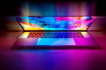 Un ordinateur portable ouvert projette des couleurs vives sur le bureau
